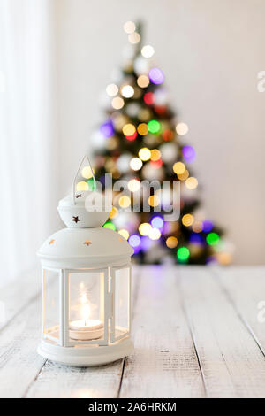 Merry Christmas! White candlestick flashlight stands on the background beautiful blurred christmas tree with luminous garland. Selective focus. Stock Photo
