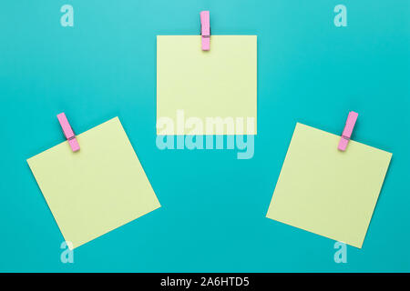 Sticky note with pink pin on turquoise background. Yellow stickers on a green background, top view. Blank notes on notice board. Blank stickers on clo Stock Photo