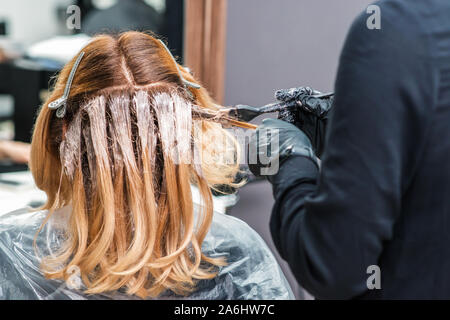 Hairdresser in black gloves is dyeing a woman's hair. Hairdresser is applying color cream at hair. Painting hair. Stock Photo