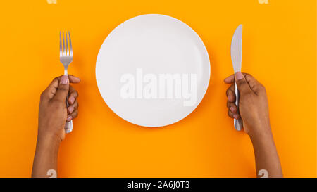 Empty plate and cutlery in woman's hands on orange background Stock Photo
