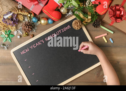 Kid writing New year resolution on black board with decorations and gift boxes, New year and Merry christmas goal  conceptual Stock Photo