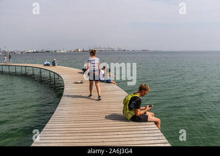 People walking by the The Infinite Bridge (Den Uendelige Bro) - circle shaped wooden pier built on a sea coast of a Aarhus Bay on a Varna Beach/Ballehage Beach, created by architect Niels Povlsgaard and Johan Gjødes  are seen in Aarhus, Denmark on 30 July 2019  © Michal Fludra / Alamy Live News