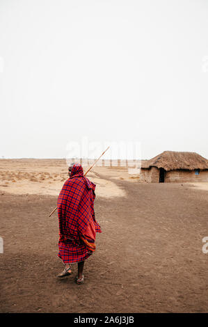 JUN 24, 2011 Serengeti, Tanzania - African Masai or Maasai tribe man in red cloth standing alone at his village in empty dusty land on cold foggy day. Stock Photo