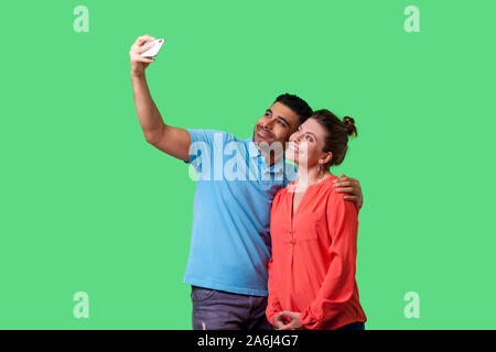 Couple doing selfie! Portrait of positive young man and woman in casual wear standing, taking pictures together using cellphone, happy memories. isola Stock Photo