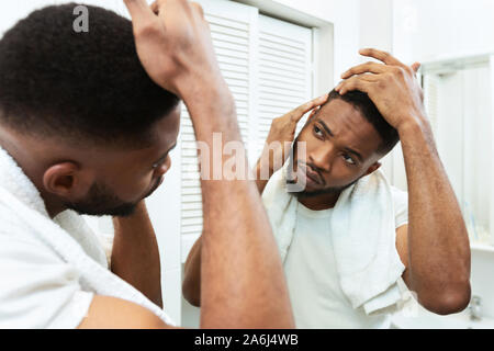Young african man checking for thinning hair in mirror at bathroom Stock Photo