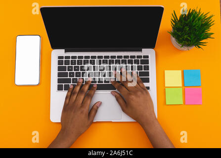 Black female hands typing on laptop over orange background Stock Photo
