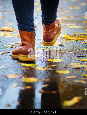 Walk on wet sidewalk. Back view on the feet of a woman walking along the asphalt pavement with puddles in the rain. Pair of shoe on slippery road in t Stock Photo