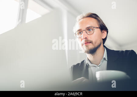 Photo of a handsome focused young man sitting by the desk working at the computer. Copy space available on the left and bottom. Stock Photo