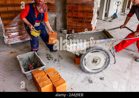 Construction workers are using their manpower to manage wheelbarrow with fresh mortar at construction site. Stock Photo