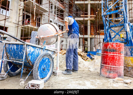Worker is pouring concrete from cement mixer into wheelbarrow. Stock Photo
