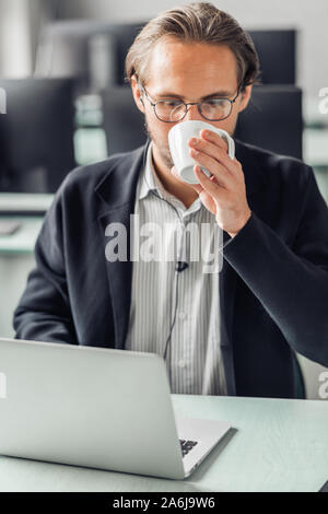 Young handsome man drinking coffee while working by the computer station. Stock Photo