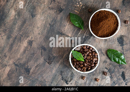 coffee beans and ground coffee in bowls with coffee tree leaf on a dark background..copy space for your text Stock Photo