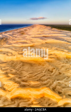 Long wide sand dunes of Stockton beach on Australian Pacific coast in aerial vertical panorama at sunrise from texture of wind work on dunes to blue s Stock Photo