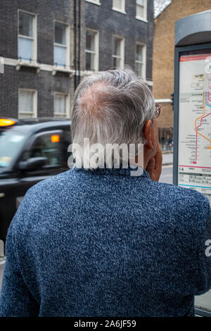 middle-aged man looking at bus time table at bus stop Stock Photo