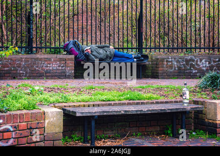 Homeless man laying on park bench Stock Photo