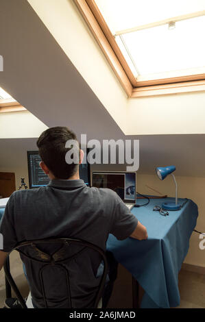 Back view of a young man working at home with computers and laptops. Concept of homeworking. Programmer working at home, programming code in monitors. Stock Photo