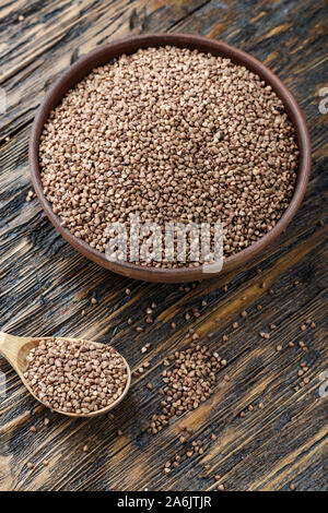 raw buckwheat in a clay plate on a wooden background. view from above. nearby lies a spoon. place for text Stock Photo