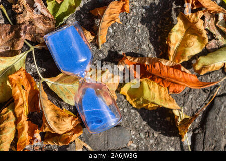 Hourglass on the pavement surrounded by autumn foliage Stock Photo
