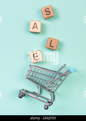 A miniature shopping cart and wooden blocks with the wordings SALE, isolated against mint background. Stock Photo