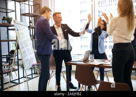 Two handsome happy businessmen shaking hands, female colleagues applauding, office workers have signed importnant contract. agreement. modern office r Stock Photo