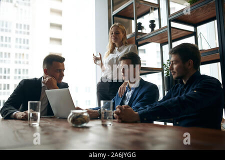 three office workers discussing a problem, while blonde woman standing behind them with a glass of water. modern office room Stock Photo