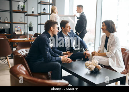 happy beautiful brunette woman talking with two handsome businessmen, guys persuading woman to collaborate with them, to be a partner Stock Photo