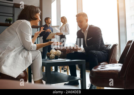young successful woman in elegant stylish suit consulting a man at workplace. free consultation, lifestyle, free time, spare time, job, profession, oc Stock Photo