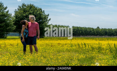 Couple standing in large field with yellow flowers and trees in the background looking at each other Stock Photo