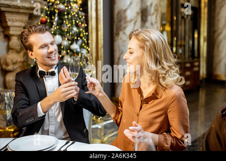 Elegantly dressed couple having a festive dinner at a well-served table, celebrating New Year holiday at the luxury interior Stock Photo