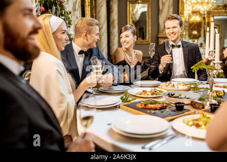 Elegantly dressed group of people having a festive dinner at a well-served table, celebrating New Year holiday at the luxury restaurant Stock Photo