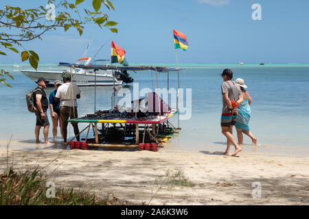 Mauritius tourists; tourists on the beach shopping from a boat stall selling gifts and souvenirs, Ile aux Benitiers, Maurtius