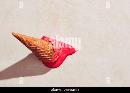 Strawberry ice cream with waffle cone dropped on the floor and melting on the ground under hot summer light. Flat lay view Stock Photo