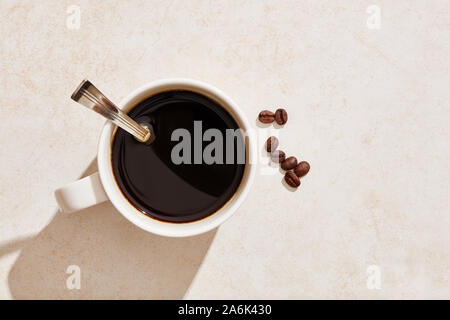 Dark black coffee in a white mug with coffee beans under harsh summer sunlight. Overhead view. Stock Photo
