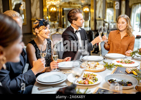 Elegantly dressed group of people having a festive dinner at a well-served table, celebrating New Year holiday at the luxury restaurant Stock Photo