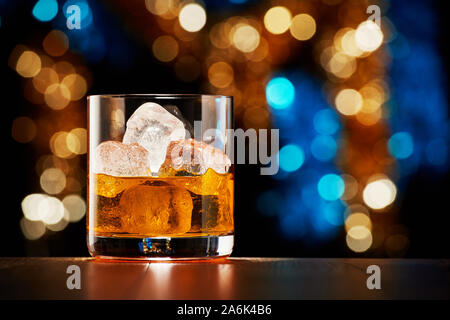 Glass of whiskey with ice on colorful Christmas lights bokeh background Stock Photo