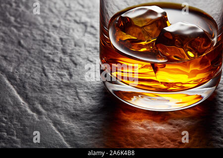 Glass of elegant whiskey with ice cubes on black stone table. Moody close up view Stock Photo