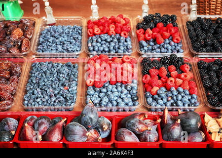 Fresh blueberries, raspberries, blackberries, figs and dry plums displayed in plastic containers on an outdoor market stall Stock Photo