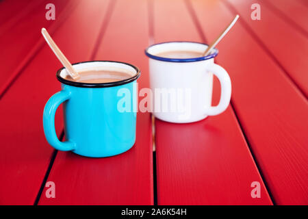 Two vintage coffee cups filled with coffee and cream on red wooden table. Morning coffee. Stock Photo