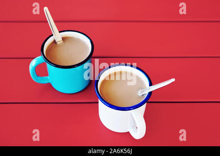 Two vintage coffee cups filled with coffee and cream on red wooden table. Morning coffee. Stock Photo