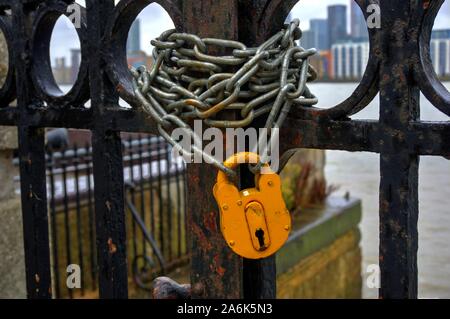 Yellow padlock and chain on wrought iron gate leading to river Stock Photo