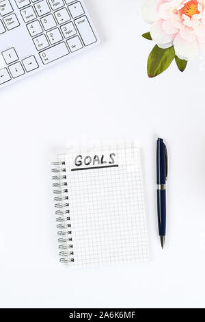 Write a goal for the new year 2020 in a white notebook on a white desktop next to a coffee mug and a keyboard. Top view, flat layout Stock Photo