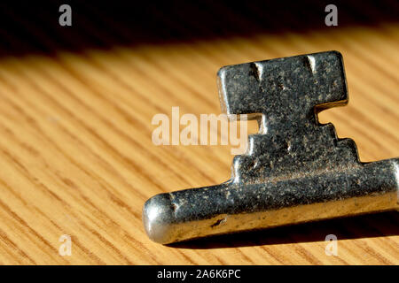 Close up of the bottom end of an old, steel key laying on a brown wooden surface in the sun. Stock Photo