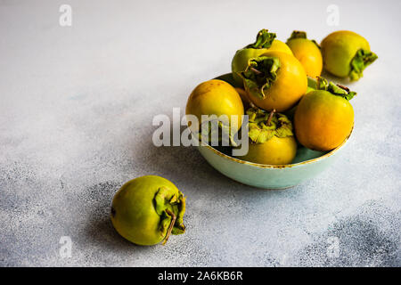 Organic food concept with ripe fresh persimmons in a bowl on stone background with copy space