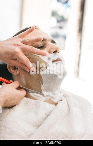 Hairdresser shaves a beard to a man with a razor in a barbershop Stock Photo