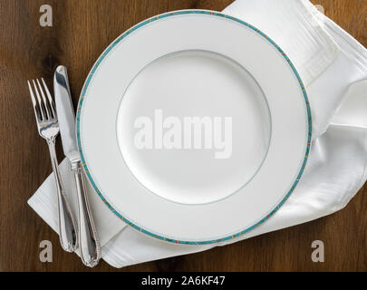 Round dinner plate with knive and fork on white napkin and wooden table flat lay Stock Photo