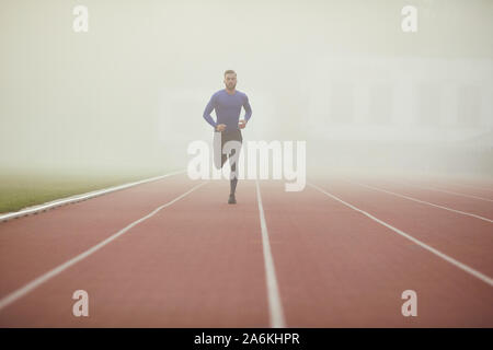 A young athlete runs on a stadium in the fog. Stock Photo