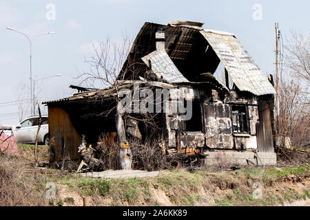 The burnt out country house is one floor, a lonely charred building. Arson Cottage, black windows, broken walls, burnt fruit tree Stock Photo