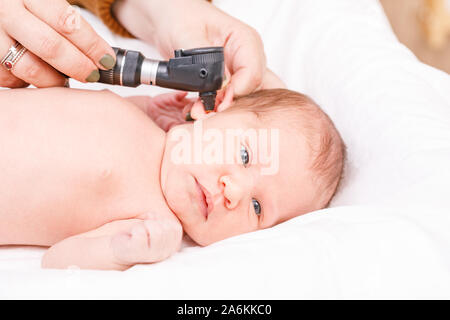 Pediatrician examines two week old baby's ear in pediatric clinic. Doctor using otoscope (auriscope) to check ear canal and eardrum membrane. Newborn Stock Photo