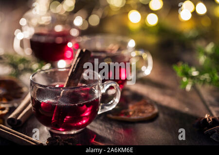 Red winter warmer drinks in a glass cups, decorated with cinnamon sticks. With string lights in the background. Stock Photo
