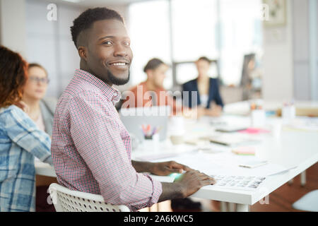 Portrait of smiling African-American man looking at camera while sitting at meeting table with creative team, copy space Stock Photo